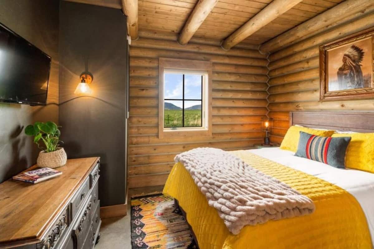 A log cabin room with a bed, a television, a window, and a painting on the wall.