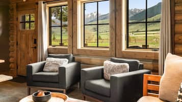 Ein Blockhausszimmer mit zwei grauen Sesseln, einem Holztisch und Blick auf Berge durch große Fenster.