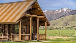 A rustic log cabin with a porch, set against a mountainous backdrop. - Copper Rose Ranch (Livingston)
