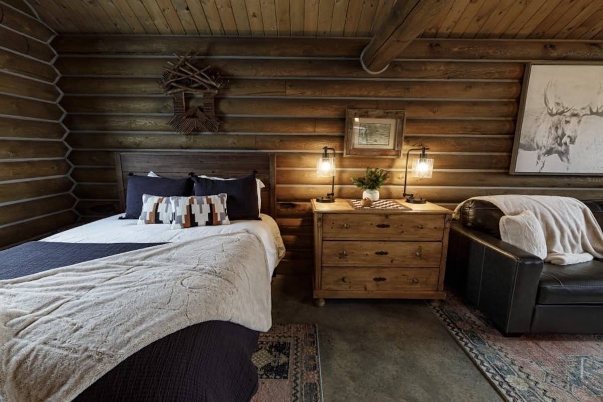 A cozy log cabin bedroom with a bed, a dresser, and a leather couch.