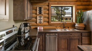 A kitchen with wooden cabinets, a stainless steel sink, a stove, and a window with a view of a building outside. - Copper Rose Ranch (Livingston)
