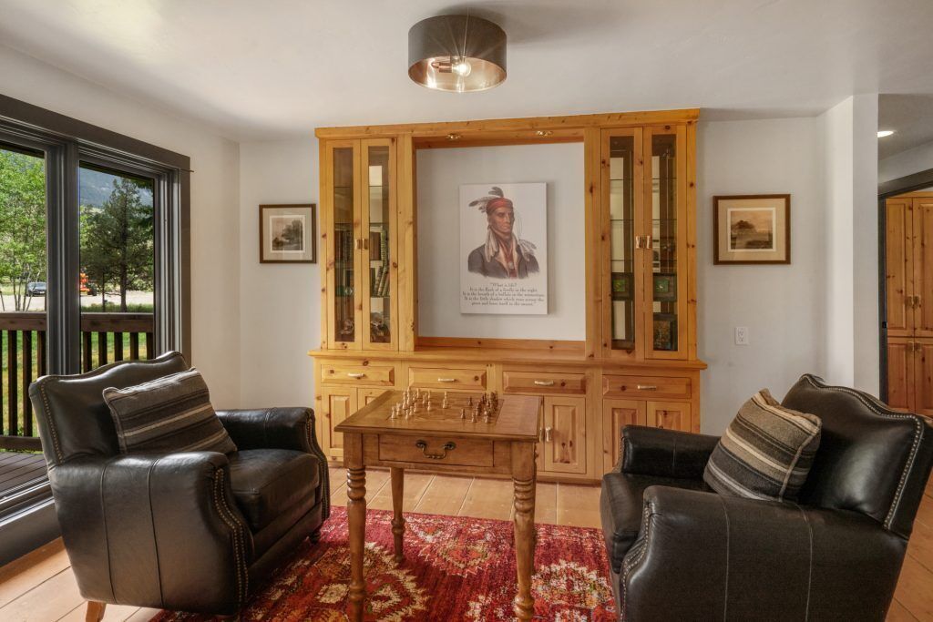 A living room with leather sofas, a wooden cabinet, a chess table, and framed pictures on the wall.