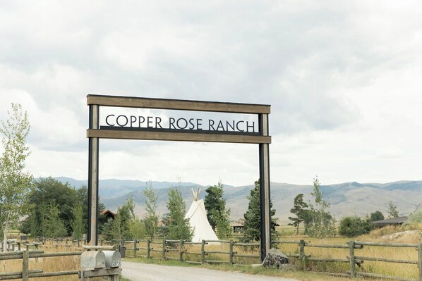 A sign for Copper Rose Ranch with a wooden fence and a teepee in the background.