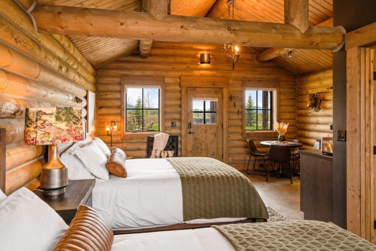 A log cabin interior with a bed, a dining table, and a fireplace.