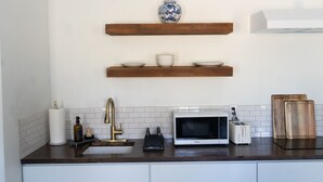 A kitchen with a white microwave, toaster, and wooden cutting boards on the counter. There are two wooden shelves above the counter, each holding bowls and a vase.