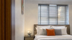 A bedroom with a bed, nightstand, and wall-mounted lamp. - Hibernate - 2 Bedroom Apartment - VI (Lagos)