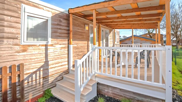 Een houten hut met een veranda, trappen die naar de veranda leiden, en een klein terras.