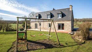 Ein Haus mit Steinaußenwand, einem großen Fenster und einer Schaukel im Garten.