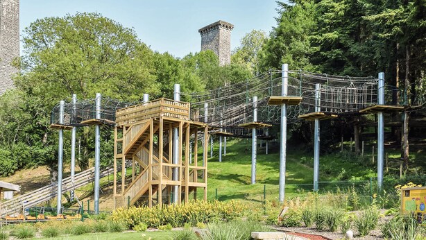 Eine Hängebrücke, Holzplattformen und ein Turm in einer Parkanlage.