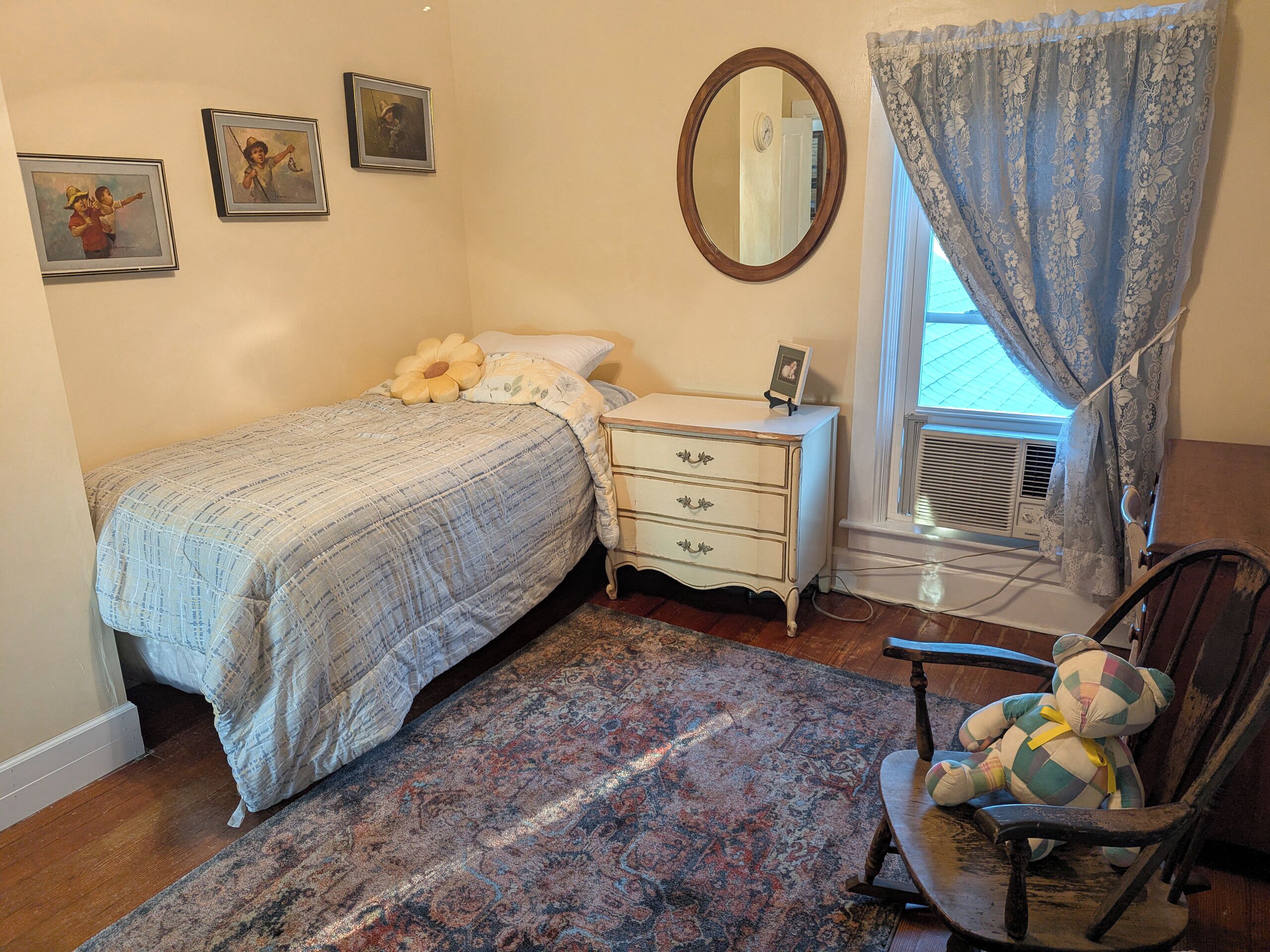 Un dormitorio con cama, cómoda, espejo y una silla con un peluche.