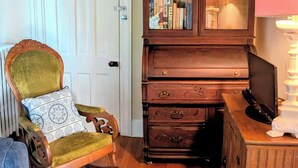 Quarto com uma cadeira de madeira com almofada estampada, um armário de madeira com portas de vidro e uma luminária sobre uma mesa de madeira.