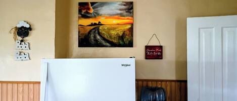 Una cocina con refrigerador, dispensador de agua y un cuadro en la pared.