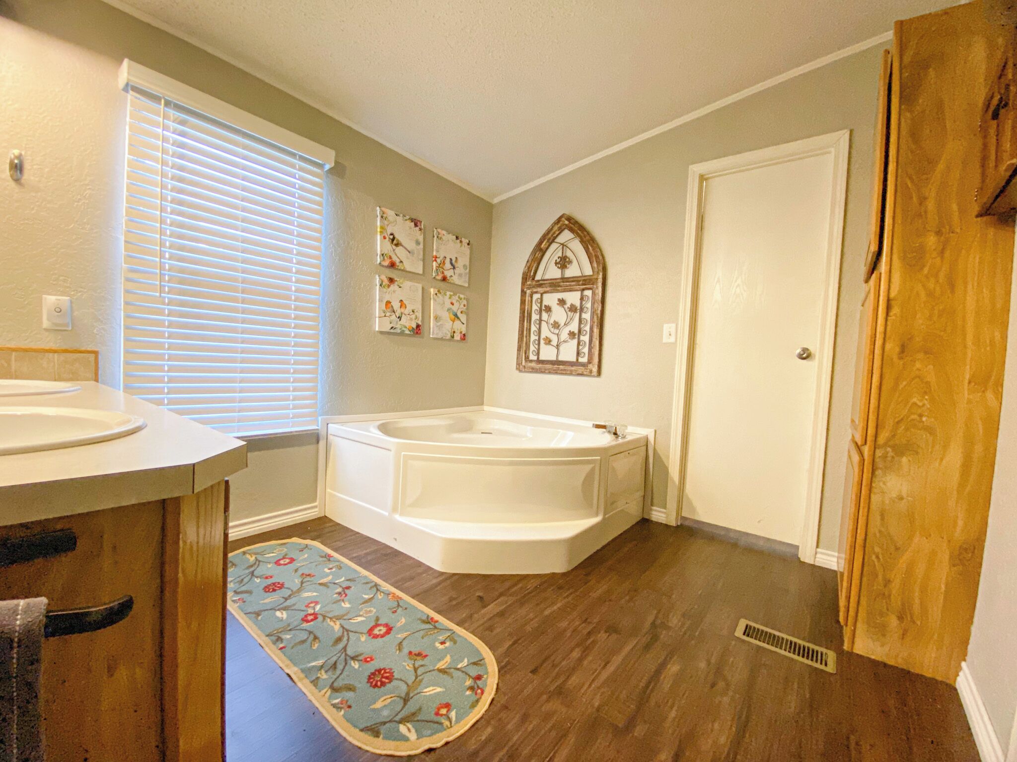A bathroom with a bathtub, two sinks, a window with blinds, and a decorative rug.
