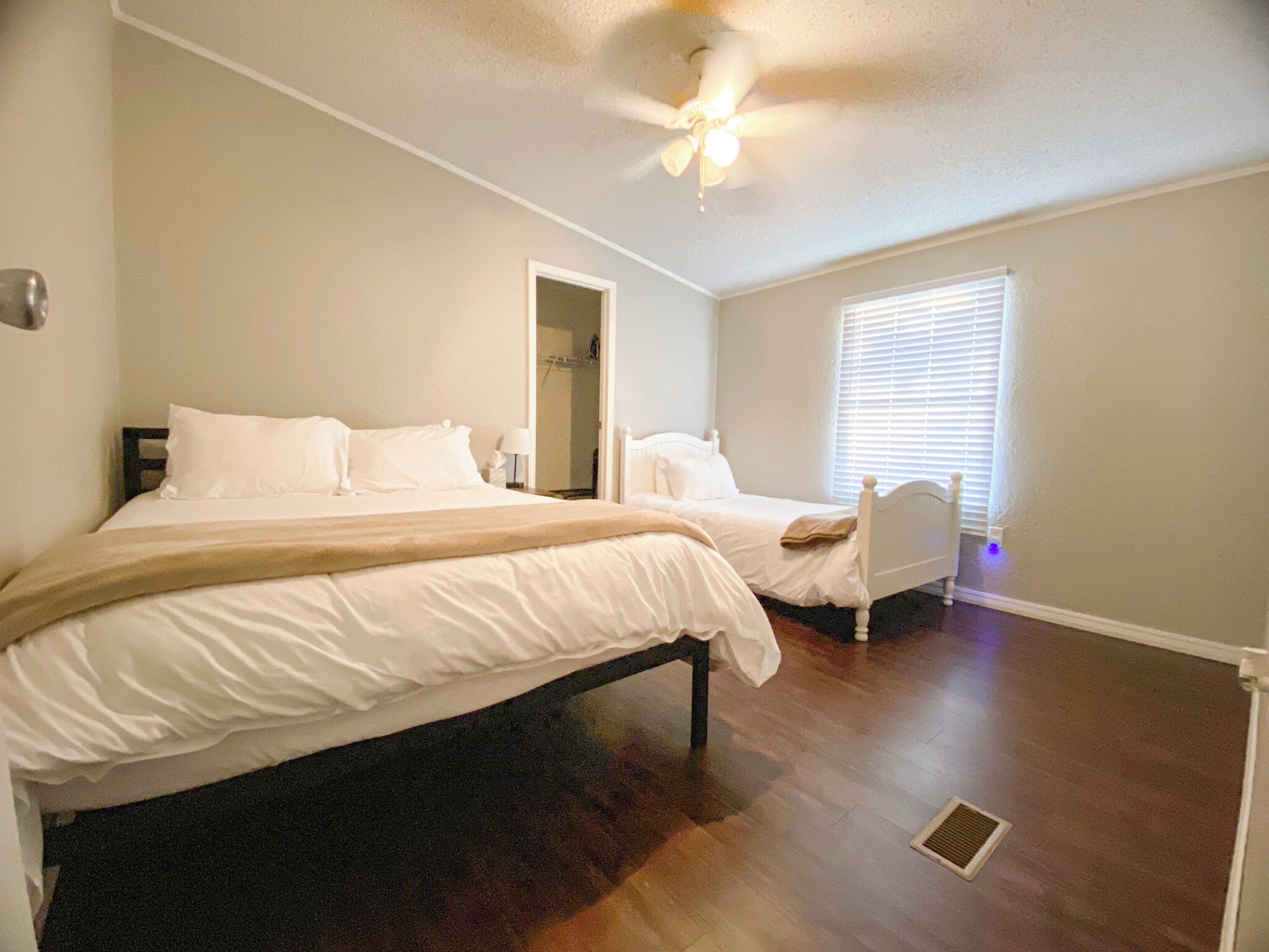 A bedroom with a large bed, a smaller bed, a ceiling fan, and a window with blinds.