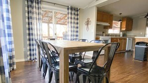 Ein Essbereich mit einem Holztisch und schwarzen Stühlen, im Hintergrund eine Küche und ein Fenster mit Vorhängen.