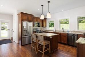 A modern kitchen with wooden cabinets, stainless steel appliances, a granite countertop, and pendant lighting. - Lakefront Cottage on Lake Leelanau | Dock, Fire Pit, Near M-22 & Dunes (Lake Leelanau)