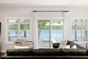 Un salon avec un canapé en cuir noir, un fauteuil et une vue sur un lac, visible à travers de grandes fenêtres.