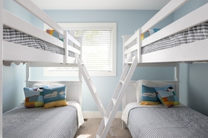 Une chambre avec des lits superposés, une fenêtre avec des stores et un petit tapis.