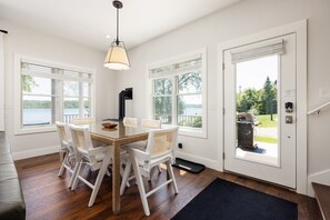 Een eetruimte met een tafel en stoelen, een zwarte kookplaat en uitzicht op een meer door grote ramen.