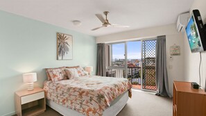 A bedroom with a bed, a ceiling fan, a TV, and a balcony with a view. - Highpoint Unit 2, 35 Maltman Street, Kings Beach (Kings Beach)