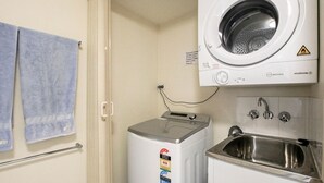 Un baño pequeño con lavadora, un lavamanos y un perchero para toallas.