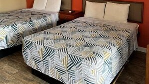 Two single beds with geometric patterned bedding, a wooden nightstand, and a red wall with framed pictures. - Holiday Motel Ocala Downtown I-75 (Ocala)
