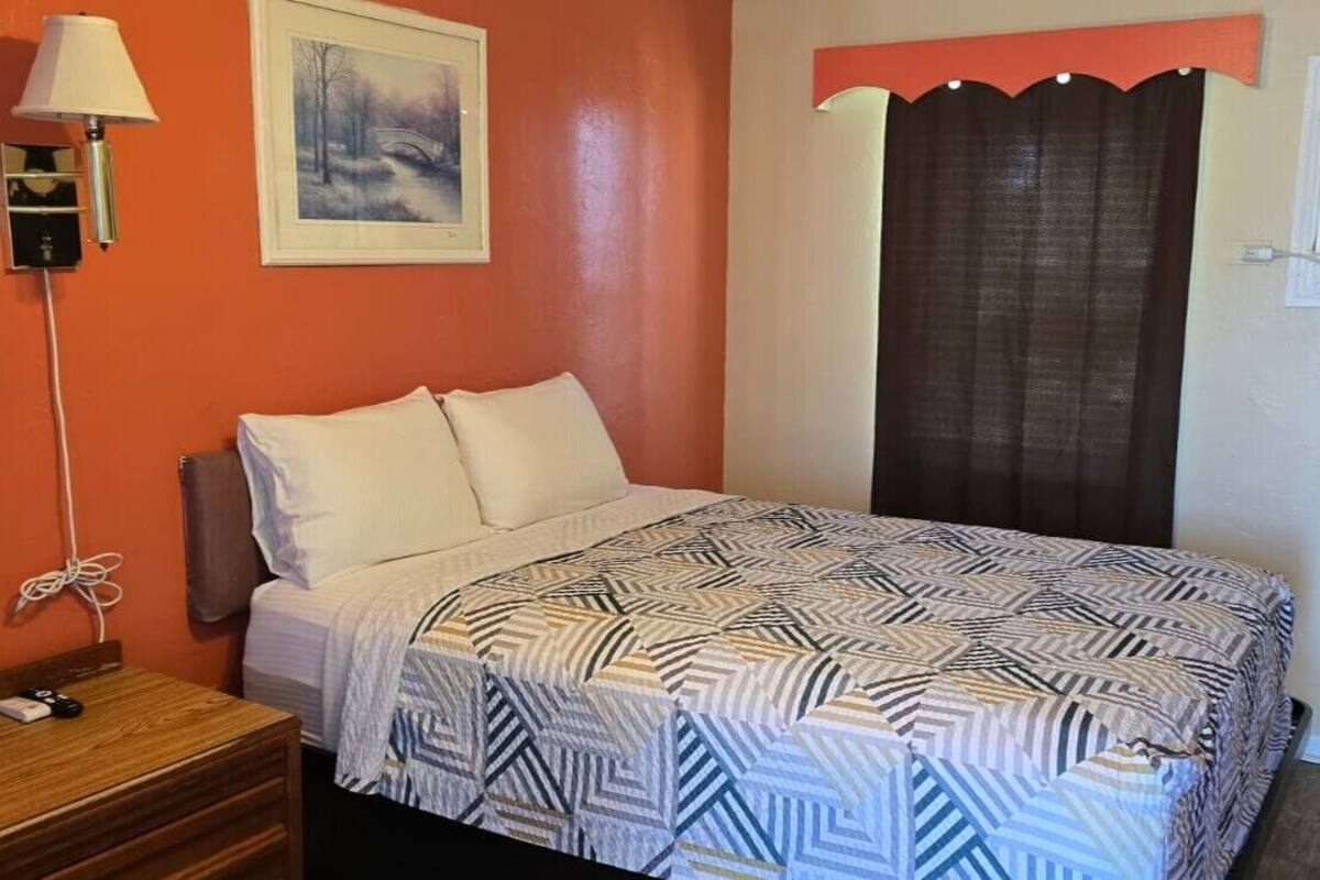 A room with a bed, a lamp, a painting, and a curtain.