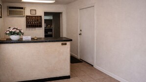 A reception area with a counter, a potted plant, a framed picture, and a door leading to a hallway. - Siesta Motor Inn Kissimmee Near Disney World (Kissimmee)