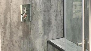 A modern bathroom with a textured wall, a glass shower enclosure, and a visible control panel. - Oyo Studio @74 (Swindon)