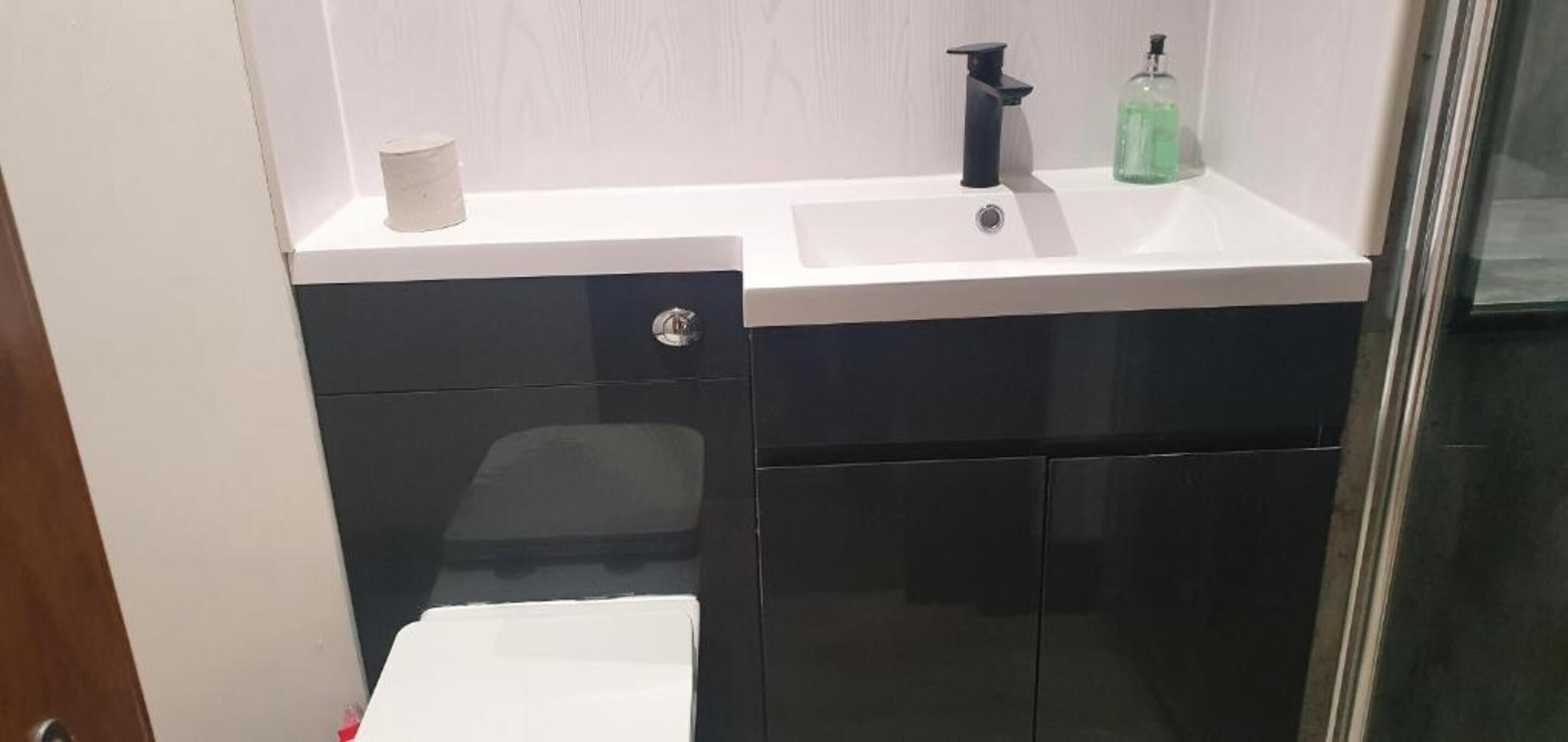 A bathroom with a white sink, black cabinet, and a glass shower enclosure.
