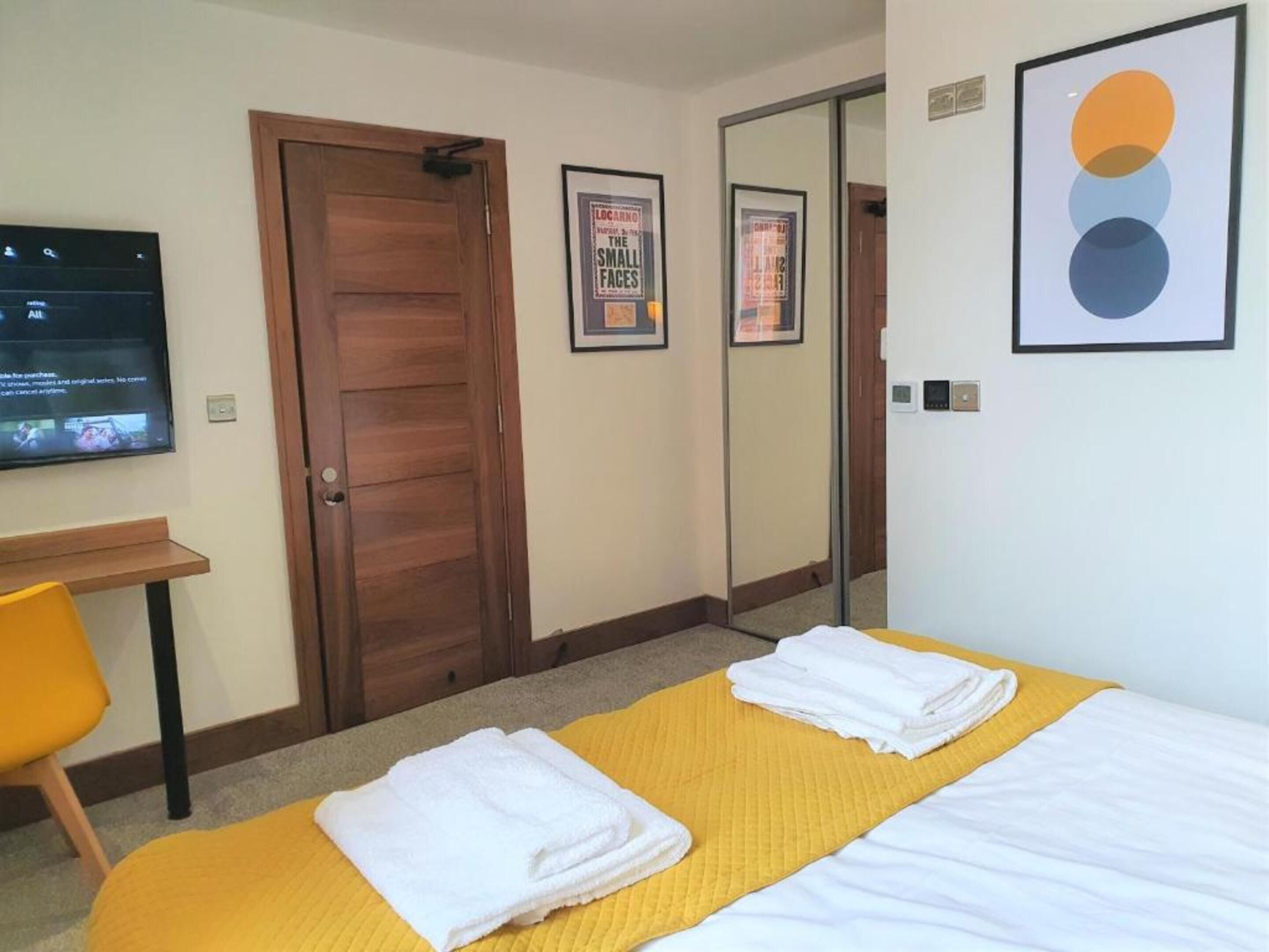 A hotel room with two beds, a desk, a TV, and a mirror.
