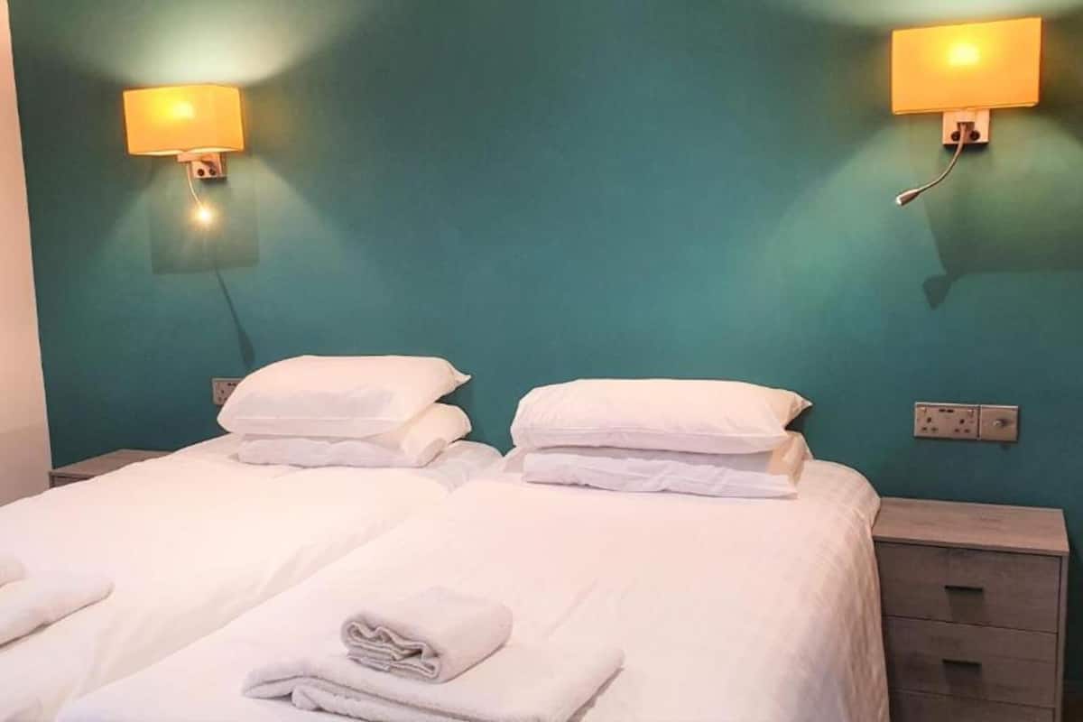 Een tweepersoonsbed met witte lakens en handdoeken, twee nachtkastjes en wandlampen.