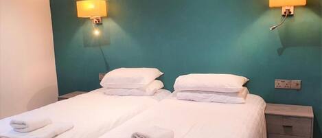 A double bed with white linens and towels, two bedside tables, and wall-mounted lamps.