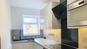 A compact kitchen with white cabinets, a black oven, and a window providing natural light. - Oyo Studio @74 (Swindon)