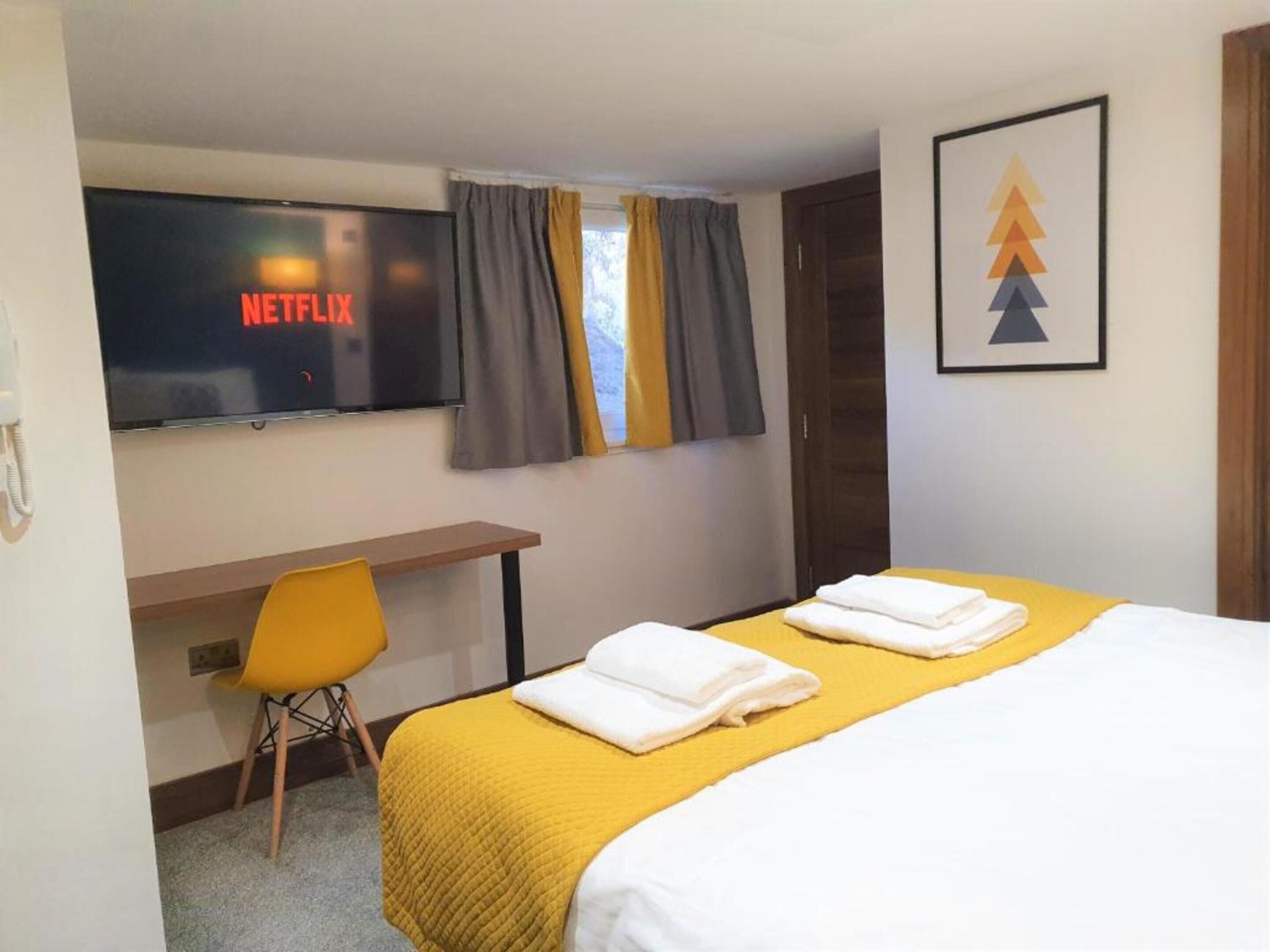 Habitación de hotel con cama, escritorio, silla, televisión mostrando el logotipo de Netflix y un cuadro en la pared.