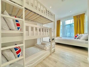 Ein Hotelzimmer mit Stockbetten, einer Schlafcouch und einem großen Fenster mit Vorhängen.