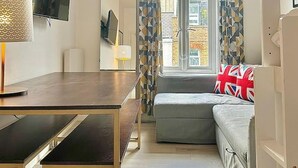 A modern living room with a sofa, a TV, and a dining table. - 10-minute Ride to Central London A (London)
