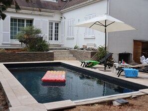 A swimming pool with a floating mat, a patio area with a table and chairs, and a covered umbrella. - Maison Le Reflet de Marne - Welkeys (Vaires-sur-Marne)