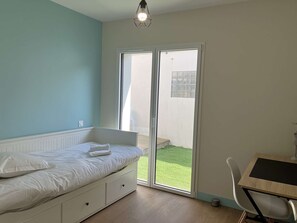 Ein Schlafzimmer mit Bett, Schreibtisch und einer Schiebetür zum Balkon.