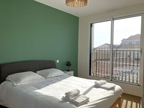 A bedroom with a bed, pillows, a nightstand, a lamp, and a view through a window. - Le Château de Sab - Saint Hilaire de Riez (SAINT HILAIRE DE RIEZ)