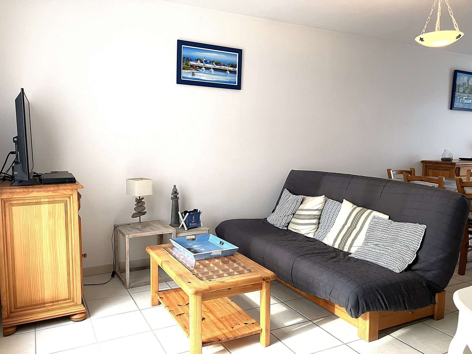 A living room with a sofa, a wooden coffee table, a television on a cabinet, a small side table with a lamp, and a framed picture on the wall.