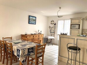 Een eethoek met een tafel voor vier personen, een houten kast en een kitchenette met een magnetron.
