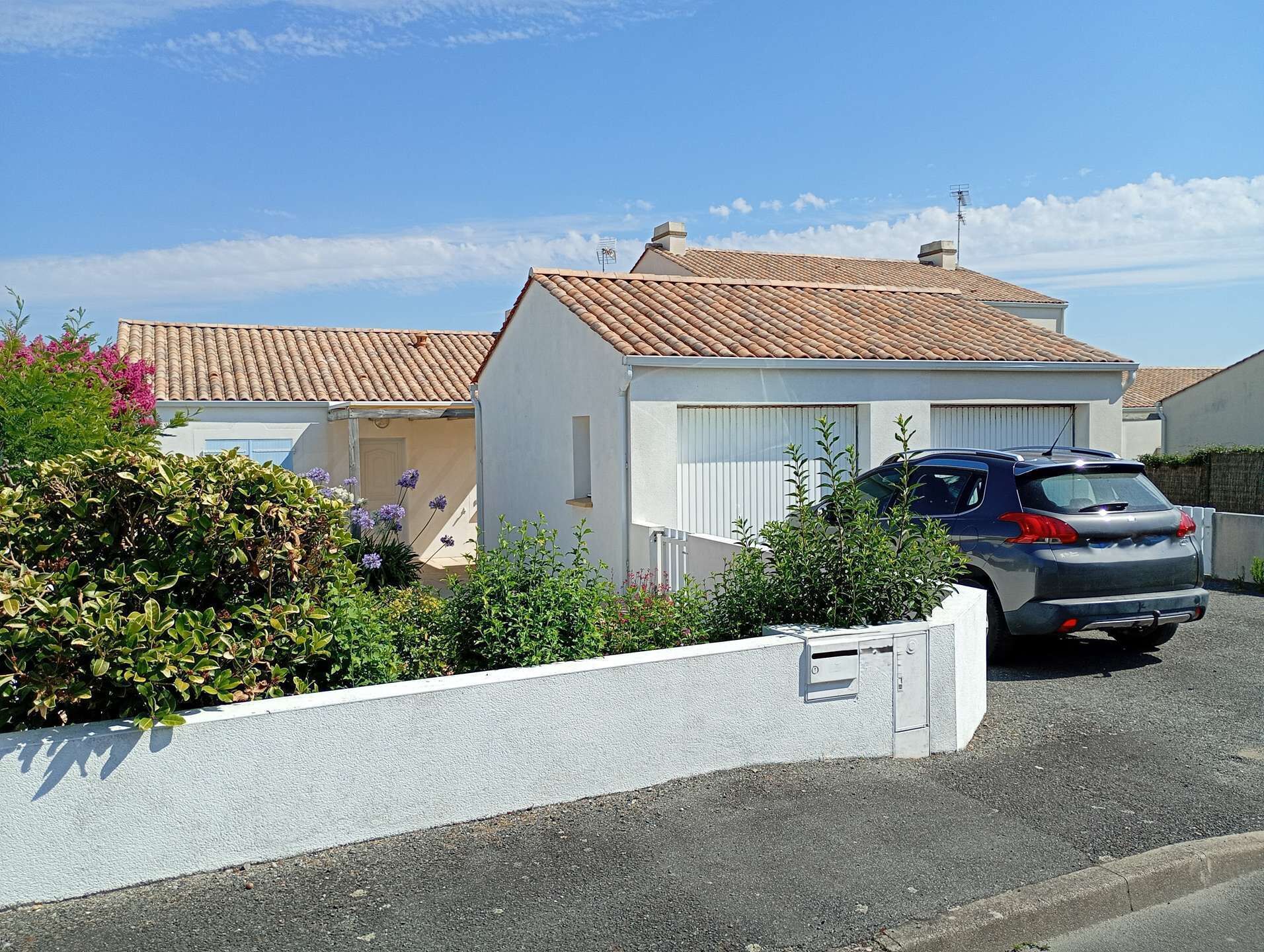 Una casa residenziale con tetto a tegole, un'auto parcheggiata e un muro bianco con una cassetta postale.