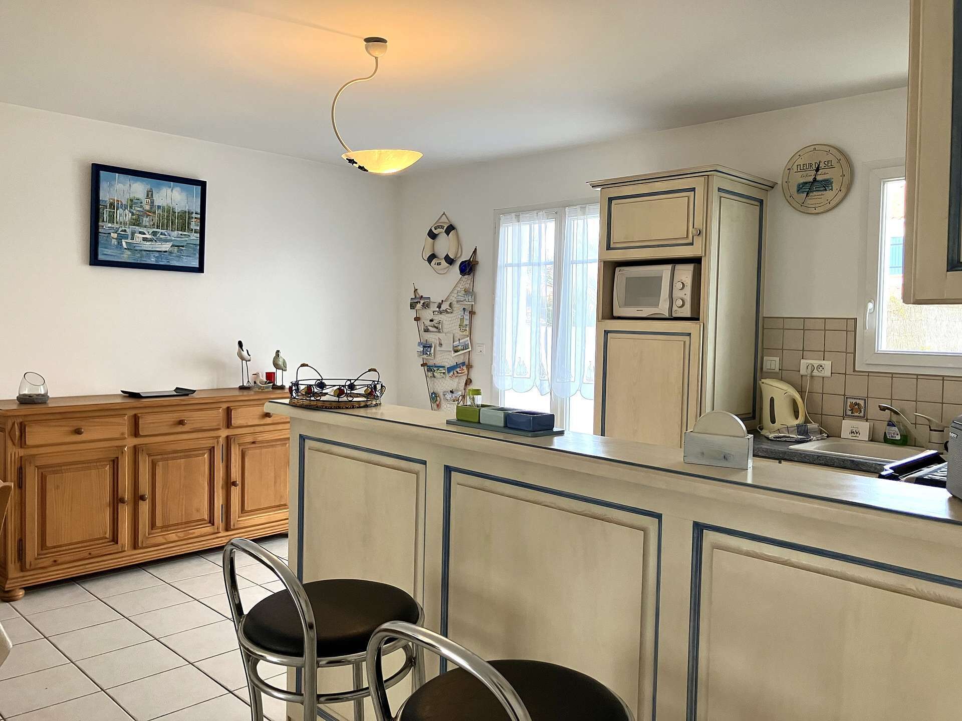 A kitchen with wooden cabinets, a microwave, and a sink. There are two bar stools and a hanging light fixture.