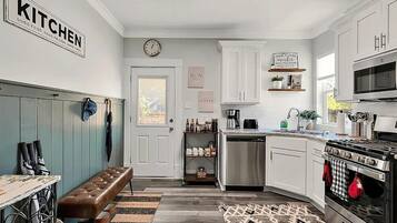 A modern kitchen with white cabinets, a built-in oven, and a coffee station.
