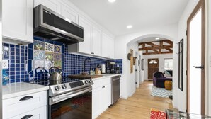 Una cocina moderna con armarios blancos, azulejos azules y electrodomésticos de acero inoxidable.