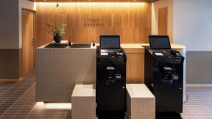 A reception desk with two computers and a plant, in a room with wooden paneling and a tiled floor. - Hotel KAN-RAKU Premier Utsunomiya-Eki (Utsunomiya)