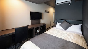 Quarto de hotel com cama, escrivaninha, TV de tela plana e ar condicionado.