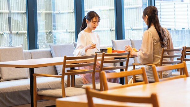 A modern dining area with wooden tables and chairs, large windows, and a city view. - Hotel KAN-RAKU Premier Utsunomiya-Eki (Utsunomiya)