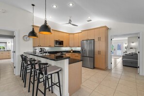 A modern kitchen with a central island, bar stools, stainless steel appliances, and wooden cabinets. - Stillpoint (Holmes Beach)